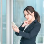 黒いスーツを着た20代の女性がスマホの画面を見ているイメージ