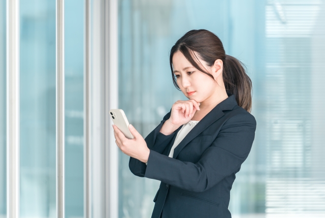 黒いスーツを着た20代の女性がスマホの画面を見ているイメージ