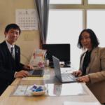 ノートパソコンを開いて向き合って座るスーツの女性と男性のイメージ